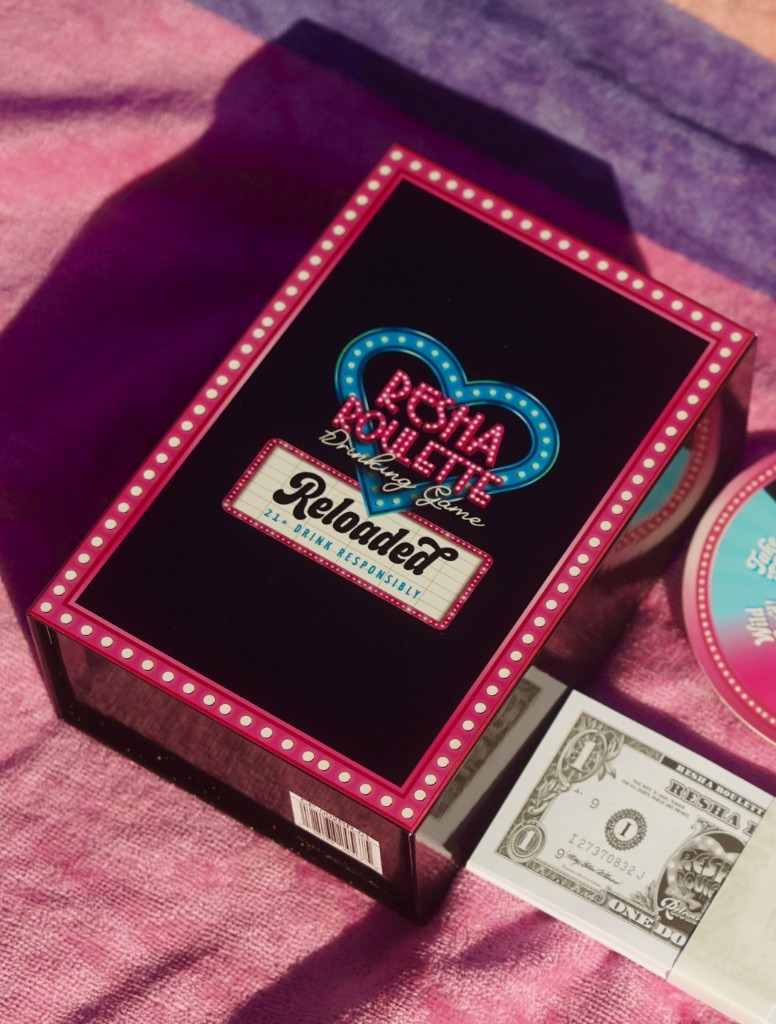 Resha Roulette Reloaded drinking game box on a pink striped towel with branded play money and marquee-style lettering.